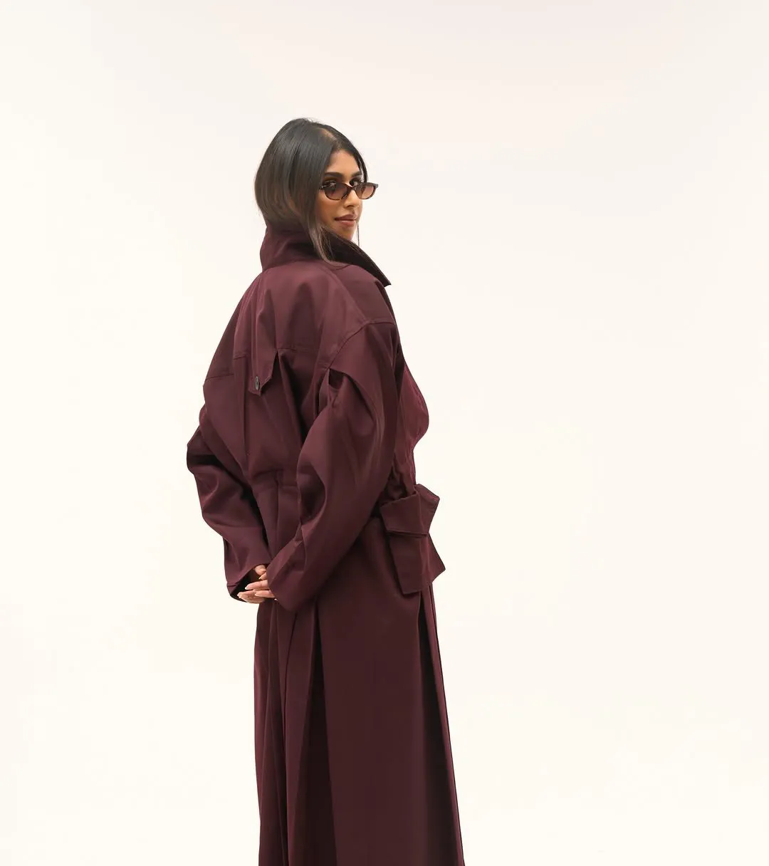 Woman looking over her shoulder in the cherry trench coat, belt flap at the waist